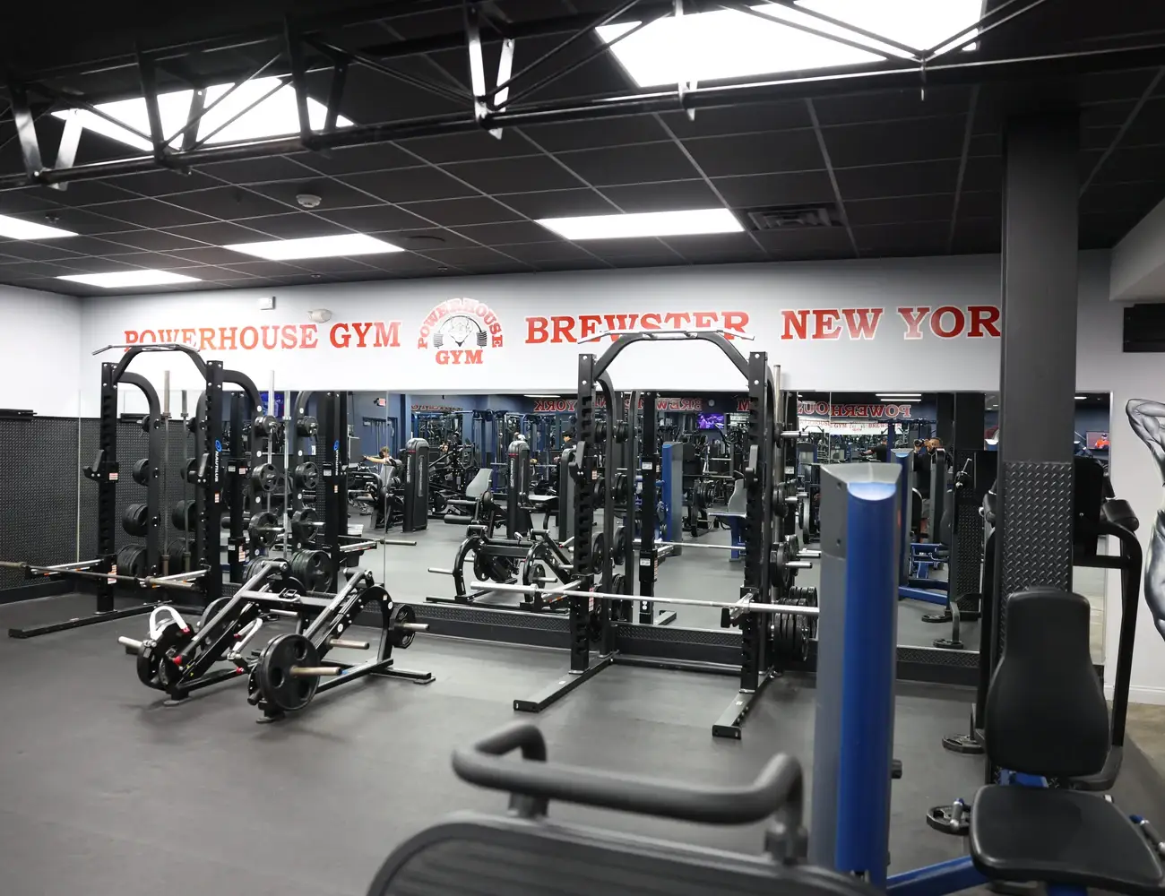 Squat racks and strength equipment beneath the Powerhouse Gym Brewster wall sign